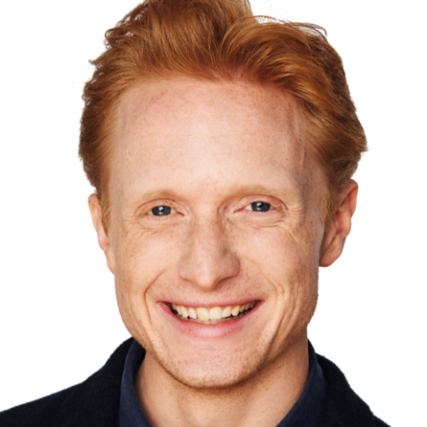 A young man with red hair, a wide smile, and deep-set dark blue eyes.